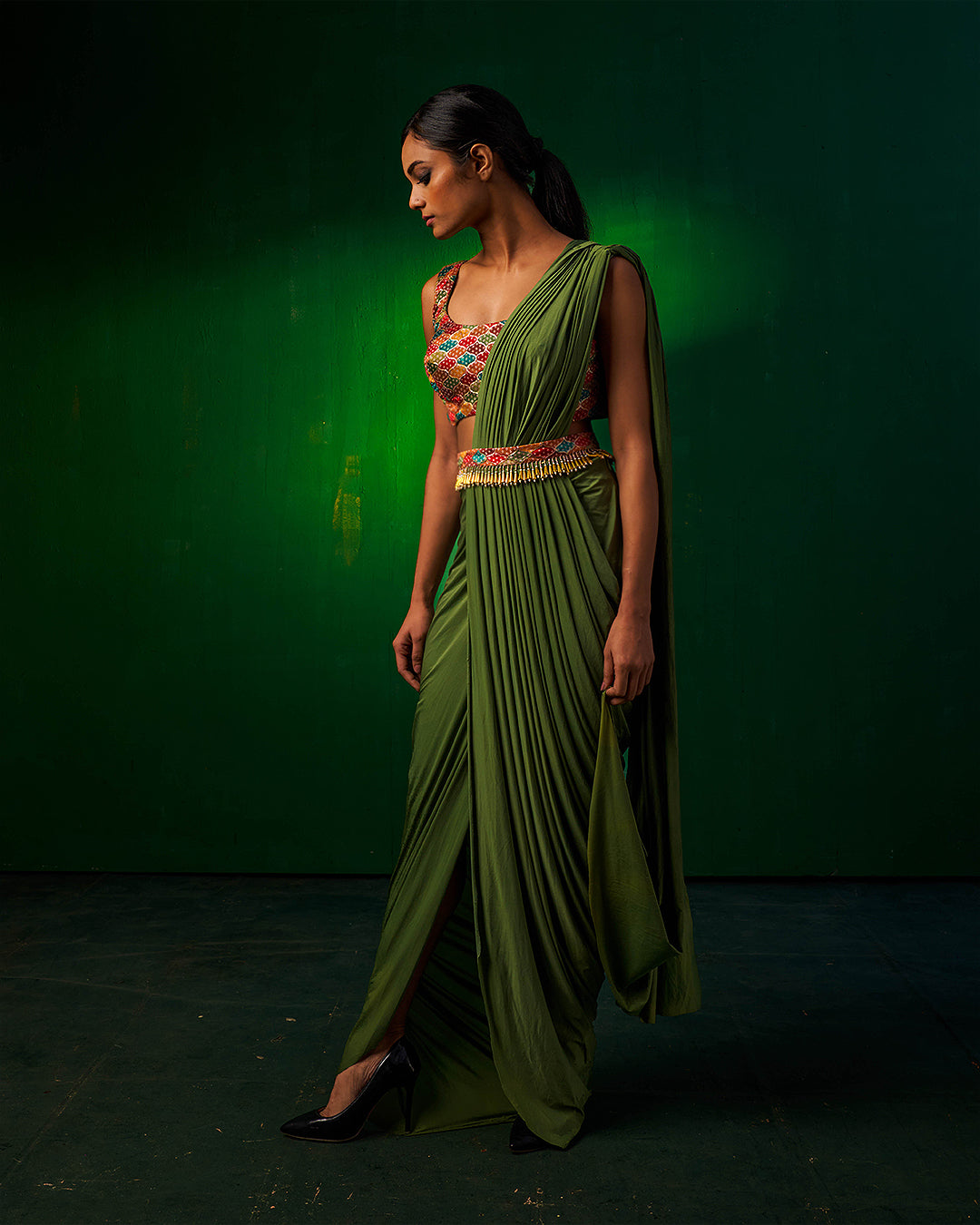 Side profile of model wearing Misakee designer green drape Indowestern saree with elegant pleats and embroidered blouse - perfect for cocktail parties and festive occasions.