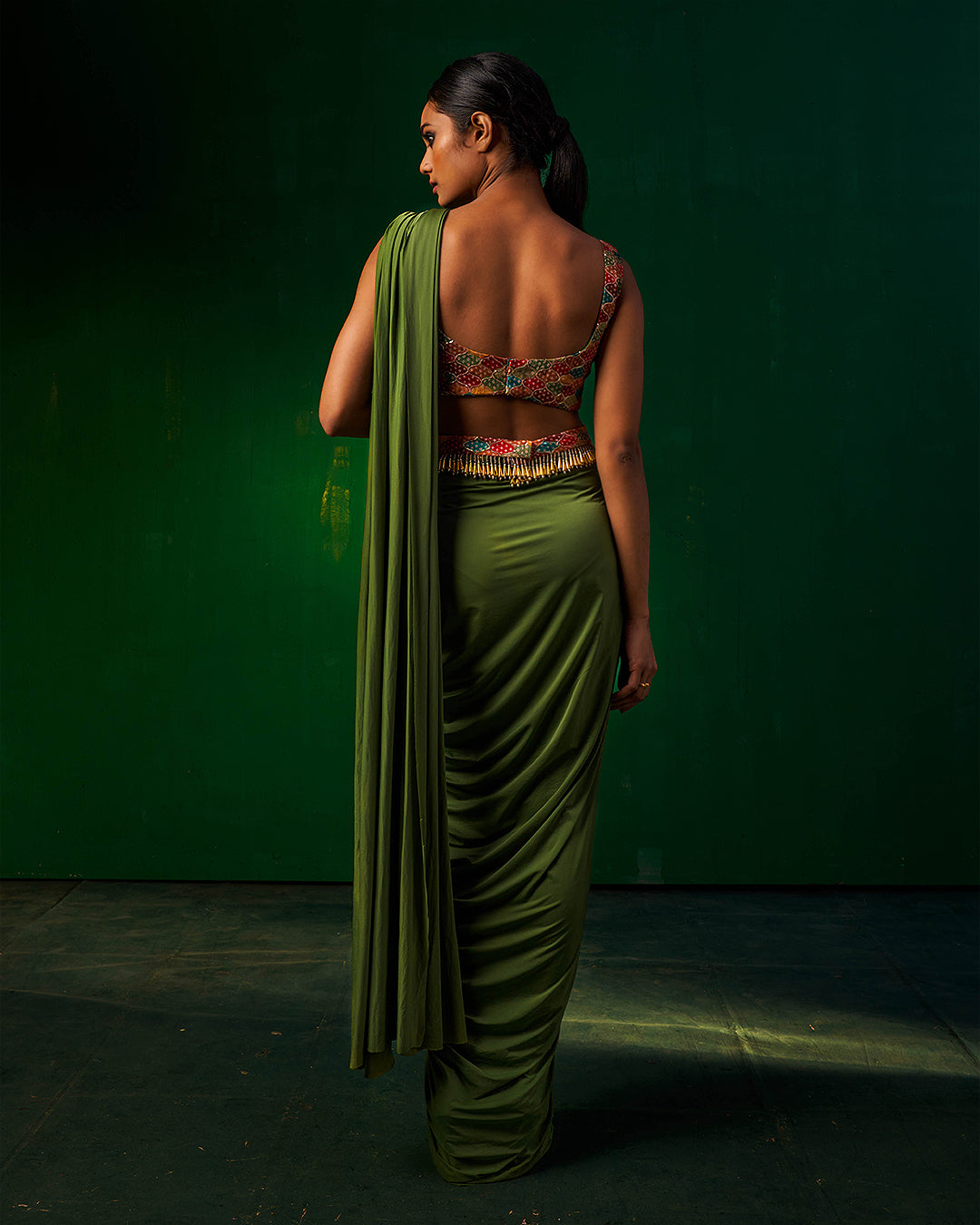 Back profile of Misakee green drape Indowestern saree highlighting the low-back embroidered blouse and sleek pleated saree drape - contemporary designer wear for festive occasions.